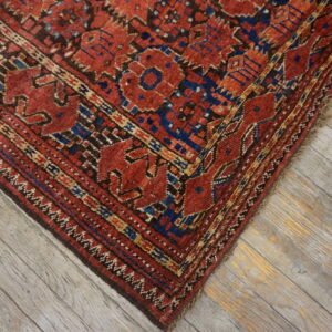Geometric red, blue, and brown patterned rug corner rests on diagonally laid gray wash wooden flooring.