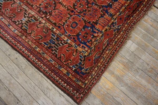 Geometric red, blue, and brown patterned rug corner rests on diagonally laid gray wash wooden flooring.