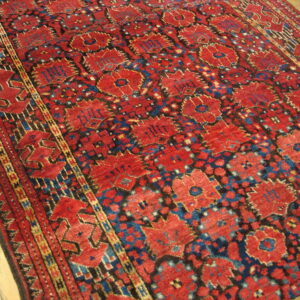 A low-pile, geometric rug in rich red, dark blue, and yellow rests on light wood planks.