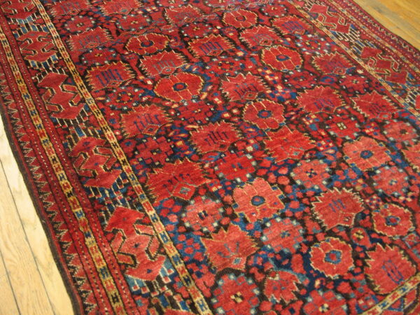 A low-pile, geometric rug in rich red, dark blue, and yellow rests on light wood planks.