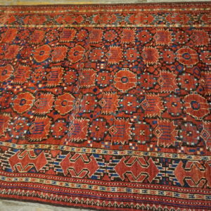 Geometric red and blue rug with detailed borders and repeating medallions lying on pale wood floors.