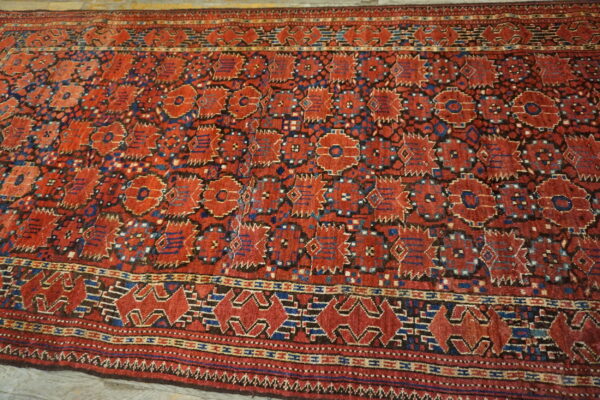 Geometric red and blue rug with detailed borders and repeating medallions lying on pale wood floors.