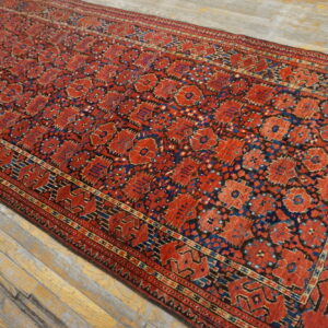A red runner rug with repeating blue and black geometric motifs lies on distressed gray wood flooring.