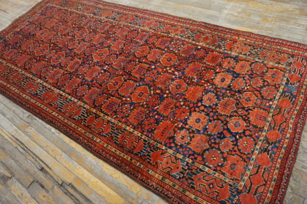 A red runner rug with repeating blue and black geometric motifs lies on distressed gray wood flooring.