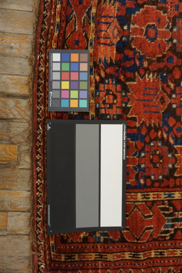 Calibration charts rest on a high-pile rug featuring red, navy, and brown geometric motifs on wood flooring.