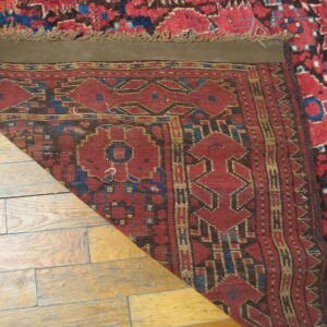 High-pile red and blue geometric rug corner folded back, revealing a flat-woven reverse on wood flooring.