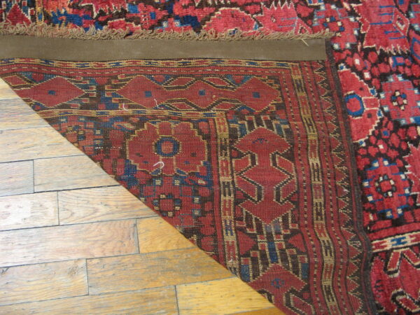 High-pile red and blue geometric rug corner folded back, revealing a flat-woven reverse on wood flooring.