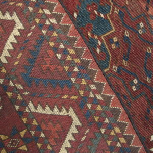 Two contrasting geometric rugs with deep red ground and patterns in blue, cream, and gold.