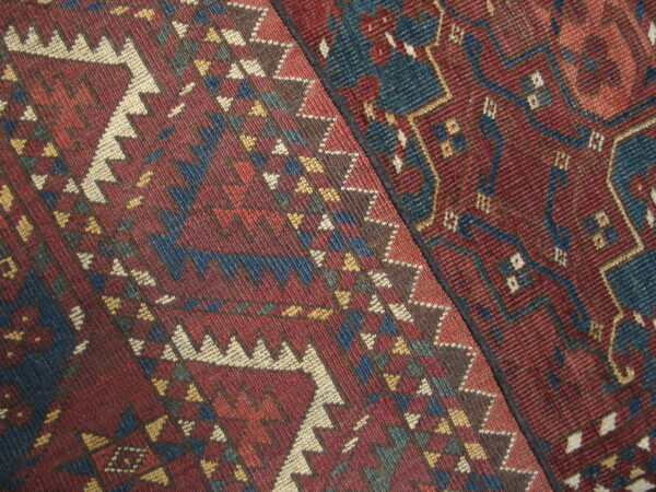 Two contrasting geometric rugs with deep red ground and patterns in blue, cream, and gold.