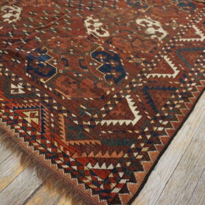 A dark red and blue geometric tribal rug with fringe lays diagonally on distressed gray wood floors.