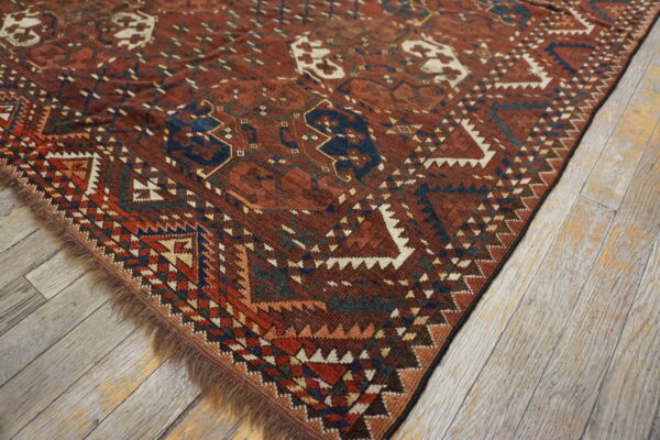 A dark red and blue geometric tribal rug with fringe lays diagonally on distressed gray wood floors.