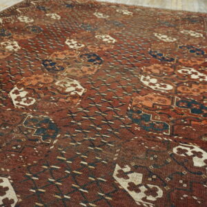 Muted red rug with dense geometric patterns in dark blue and off-white on distressed wood planks.