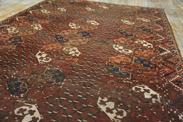 Muted red rug with dense geometric patterns in dark blue and off-white on distressed wood planks.