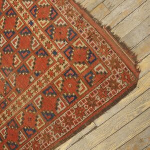 A red, blue, and cream geometric rug with low pile rests on distressed wood plank flooring.
