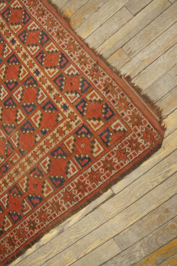 A red, blue, and cream geometric rug with low pile rests on distressed wood plank flooring.