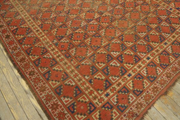 Rust-red rug with diagonal geometric shapes in blue and tan lies on distressed gray wood floorboards.