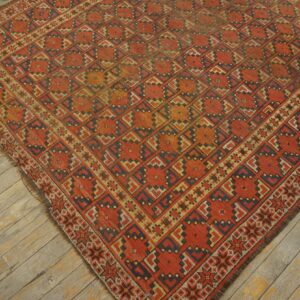 Low-pile rug with a repeating geometric medallion pattern in rust, indigo, and gold on weathered wood planks.