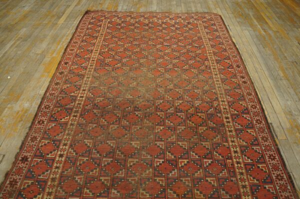 Red and blue patterned low-pile rug displayed on distressed light wood flooring.