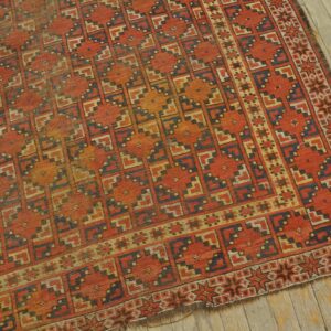Rust-colored rug with a repeating blue and tan stepped geometric pattern on distressed wood flooring.