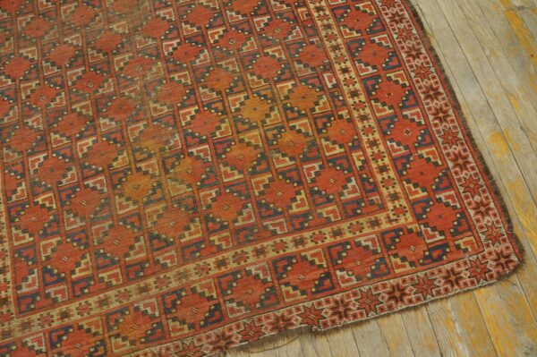 Rust-colored rug with a repeating blue and tan stepped geometric pattern on distressed wood flooring.