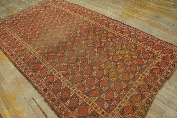 Red and navy geometric area rug with low pile rests on rustic, worn hardwood planks.