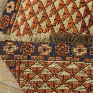 The rust and cream geometric rug is folded, showing the woven pile and foundation on wood planks.