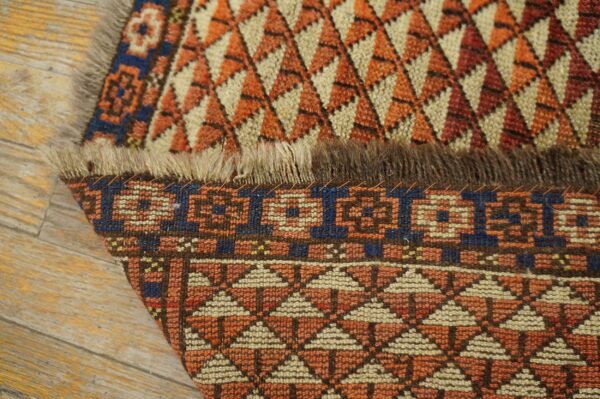 The rust and cream geometric rug is folded, showing the woven pile and foundation on wood planks.