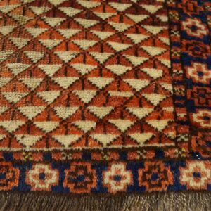 A close-up view of a shaggy rug with orange geometric patterns and a blue and cream floral border.