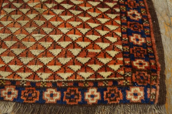 A close-up view of a shaggy rug with orange geometric patterns and a blue and cream floral border.