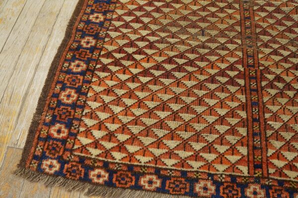 A geometric rug featuring alternating orange, rust, and tan triangles, with a blue border on wood flooring.