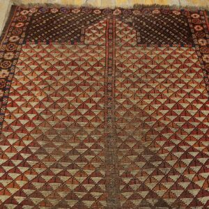 Geometric rug with repeating orange and tan triangles, a dark border, and light distressed wood flooring.
