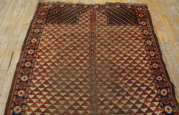Geometric rug with repeating orange and tan triangles, a dark border, and light distressed wood flooring.