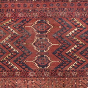 Low pile rug with red and navy geometric motifs, chevron bands, and triple diamond medallions.