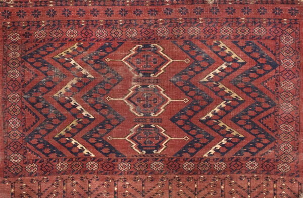 Low pile rug with red and navy geometric motifs, chevron bands, and triple diamond medallions.