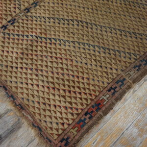 Rustic beige rug with small red and blue geometric patterns rests on gray-washed, distressed hardwood flooring.