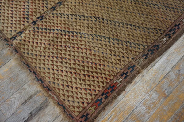 Rustic beige rug with small red and blue geometric patterns rests on gray-washed, distressed hardwood flooring.