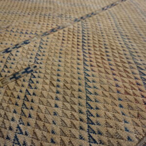 Close-up showing a textured tan rug with dense rows of small dark blue triangular patterns.
