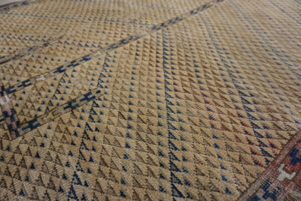 Close-up showing a textured tan rug with dense rows of small dark blue triangular patterns.
