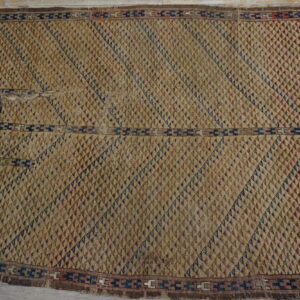 Textured tan and brown rug with raised diamond shapes and navy geometric borders on a distressed wood floor.