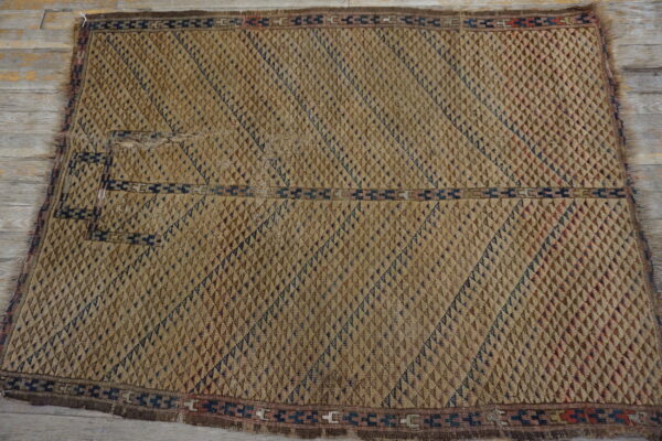 Textured tan and brown rug with raised diamond shapes and navy geometric borders on a distressed wood floor.