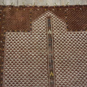 A geometric brown and cream rug featuring an arch motif is displayed on rustic wood planks.