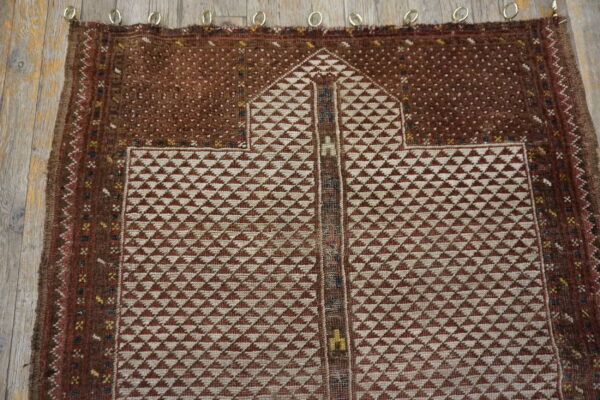 A geometric brown and cream rug featuring an arch motif is displayed on rustic wood planks.