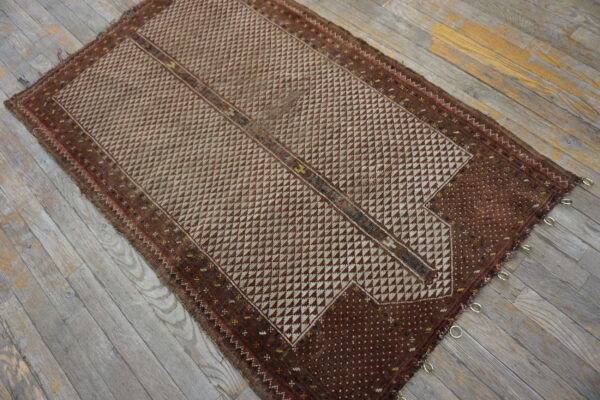 Geometric brown and cream rug with metal rings visible on one edge lies on weathered plank wood flooring.