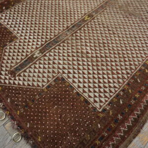 Geometric brown and cream rug with low pile, metal rings attached, lying on grey wood floor.