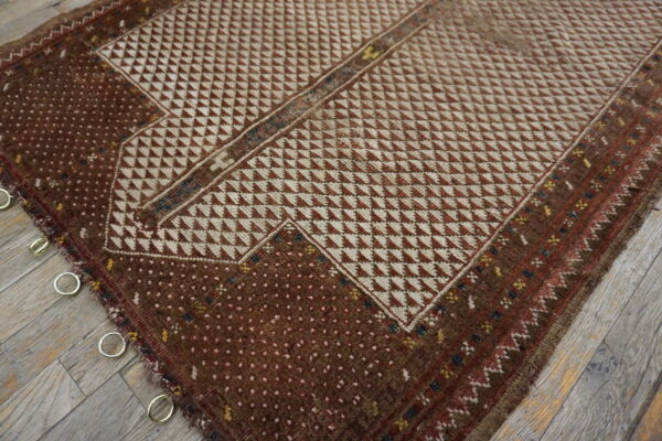 Geometric brown and cream rug with low pile, metal rings attached, lying on grey wood floor.