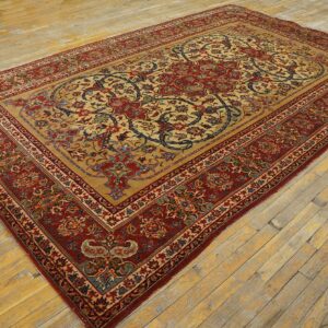 Red and tan floral traditional rug with blue accents displayed on worn, wide plank wood flooring.