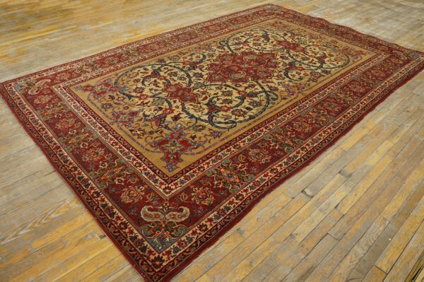 Red and tan floral traditional rug with blue accents displayed on worn, wide plank wood flooring.