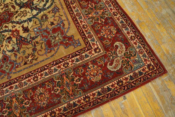 Close-up of a traditional gold and tan rug with red, blue, and cream floral borders on distressed yellow wood flooring.