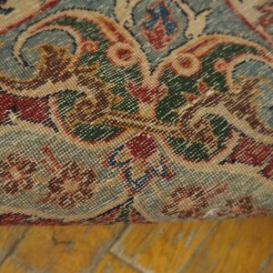 Ornate, low-pile rug detail showing muted red, sage, green, and tan colors rolled over a yellow wood floor.