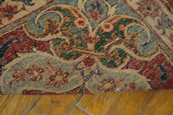 Ornate, low-pile rug detail showing muted red, sage, green, and tan colors rolled over a yellow wood floor.